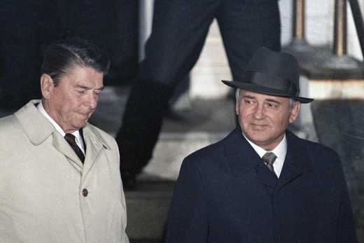 President Ronald Reagan stands on the left and Soviet President Mikhail Gorbachev stands on the right. Reagan is wearing a tan overcoat. Gorbachev is wearing a black overcoat and hat.