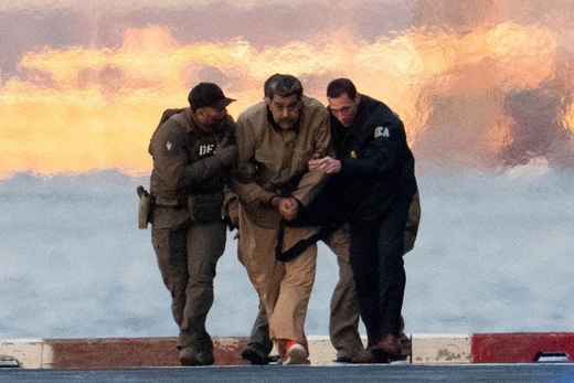 Two officers flank ousted Venezuelan leader Nicolás Maduro as they walk across the pavement.
