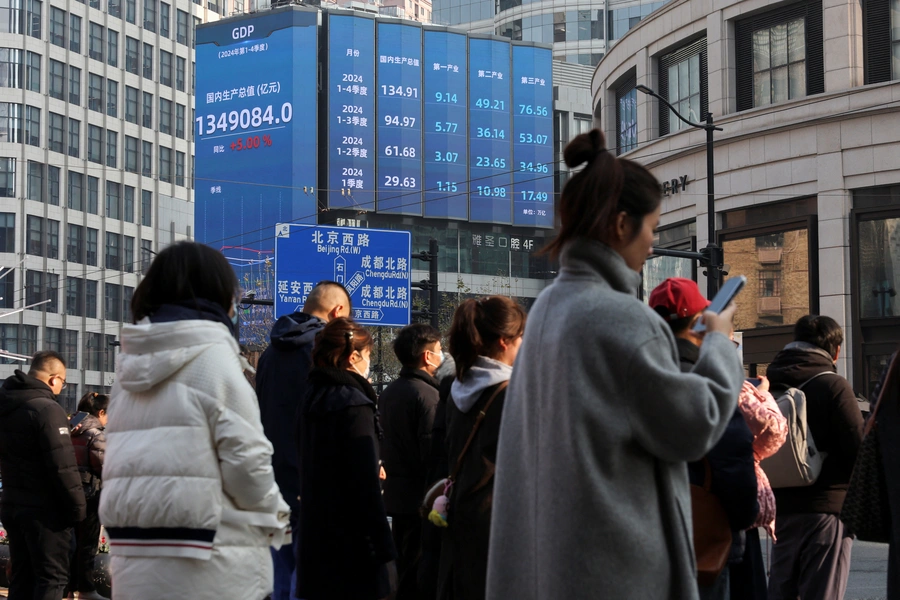 Pedestrians wait for a street signal on a sidewalk as an electronic billboard shows China's 2024 GDP growth in Shanghai, China January 21, 2025. Go Nakamura/Reuters