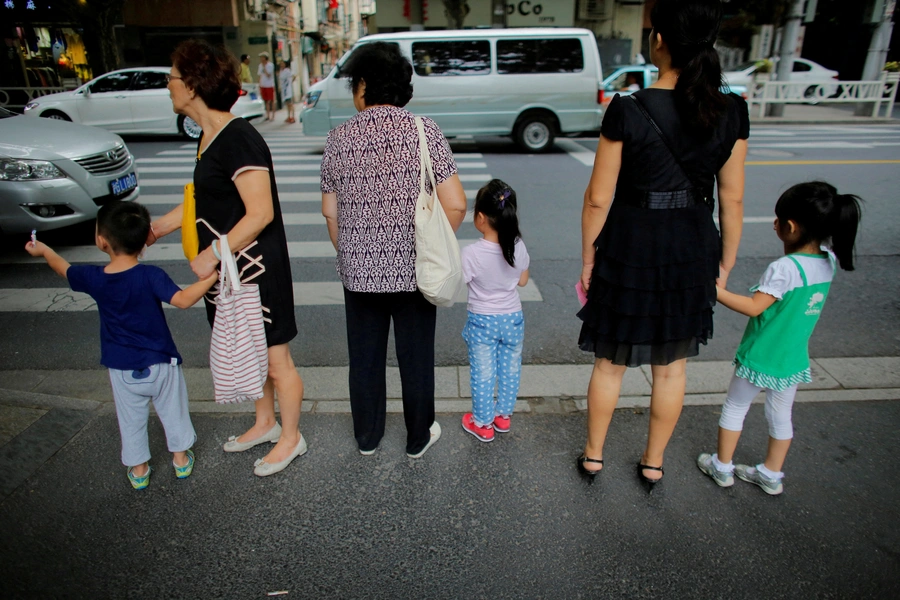 Women hold childrens' hands as they wait to cross a street after school in downtown Shanghai, China September 12, 2014. REUTERS/Carlos Barria