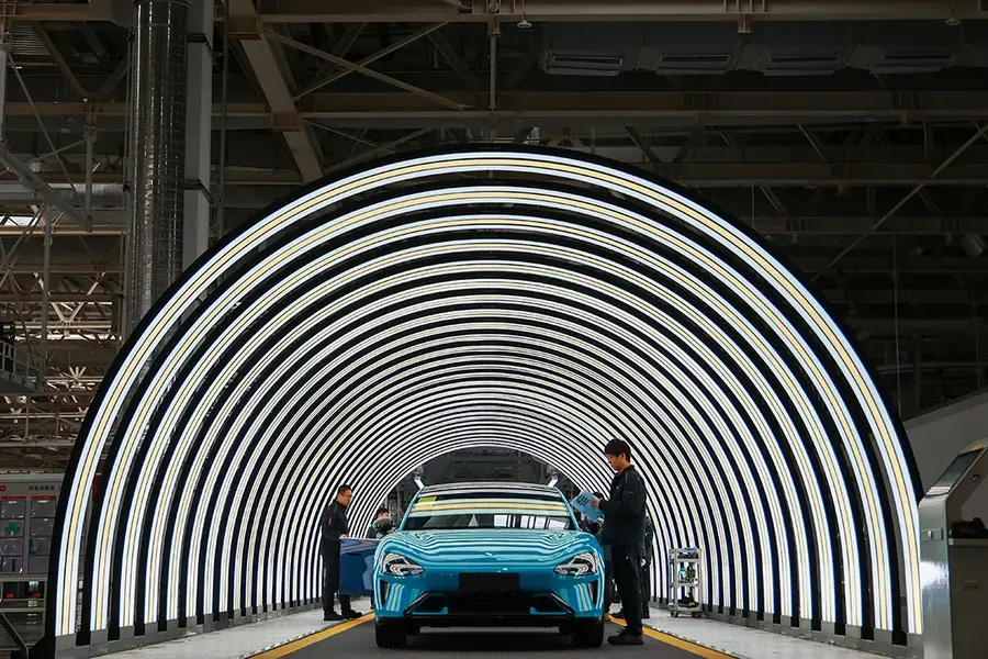 A blue car under an illuminated futuristic semicircle of beams.