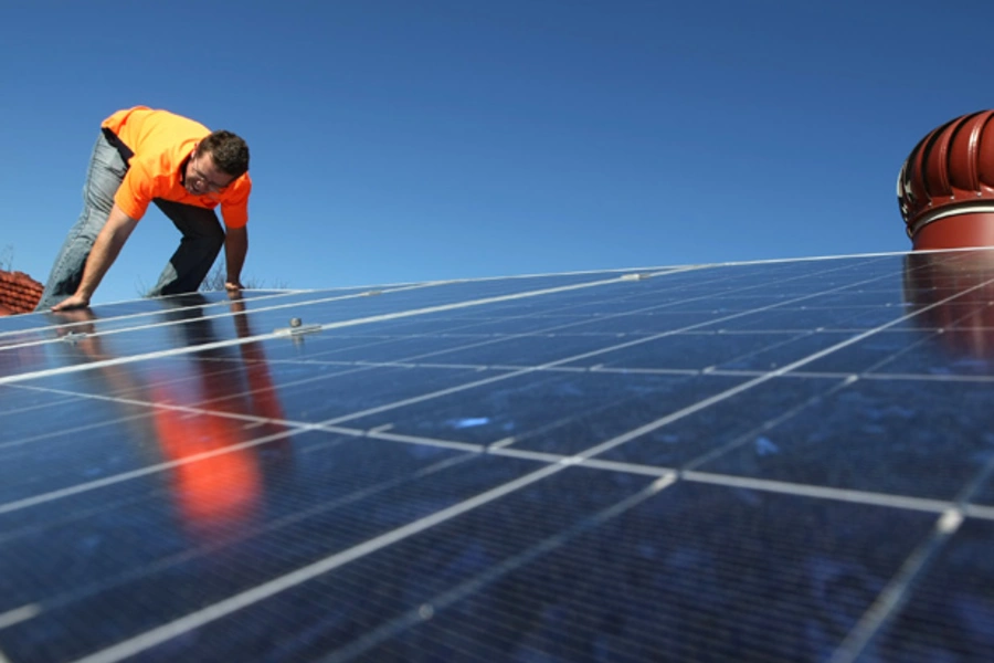 A solar system installer adjusts new solar panels on the roof of a house (Tim Wimborne/Courtesy Reuters).