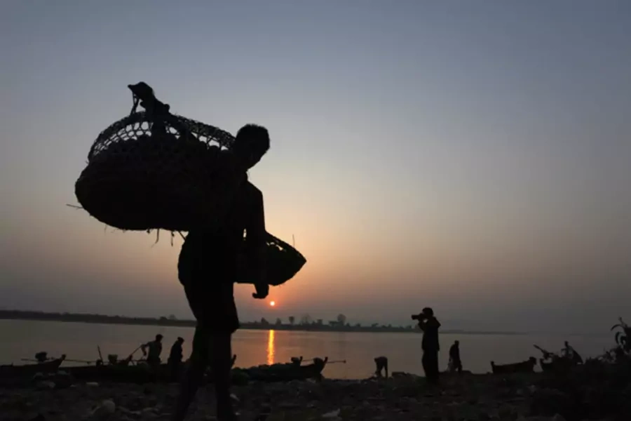 A Burmese man unloads tomatoes from a small boat along the Irrawaddy river banks. Some analysts worry about the consequences of a gluttony of foreign investment in Myanmar.