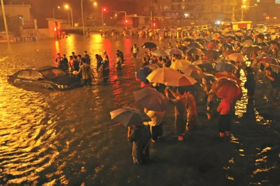 Rescuers and residents stand next to a stranded car which is being pulled up from a flooded street under the Guangqumen overpass amid heavy rainfalls in Beijing on July 21, 2012.