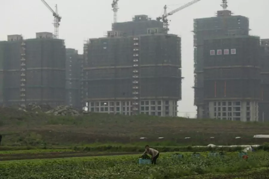 A farmer works in her field in front of a residential construction site in Shanghai on April 25, 2012.