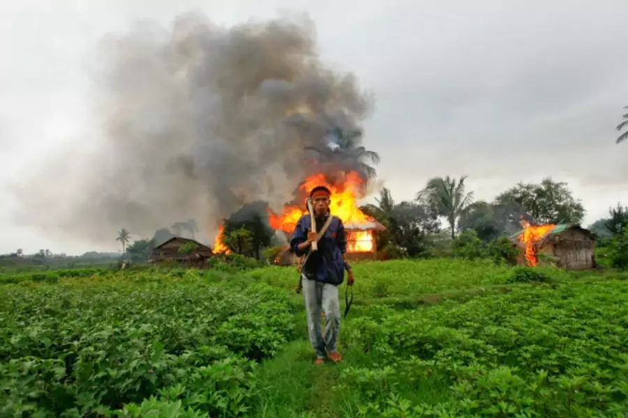 An ethnic Rakhine man holds homemade weapons as he walks in front of houses that were burnt during fighting between Buddhist Rakhine and Muslim Rohingya communities in Sittwe on June 10, 2012.