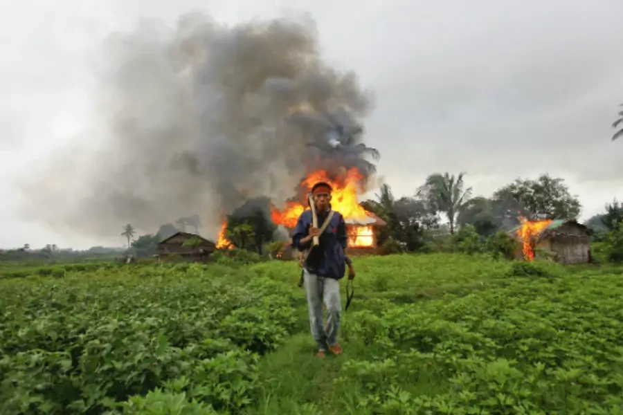 An ethnic Rakhine man holds homemade weapons as he walks in front of houses that were burnt during fighting between Buddhist Rakhine and Muslim Rohingya communities in Sittwe on June 10, 2012. (Courtesy Reuters)