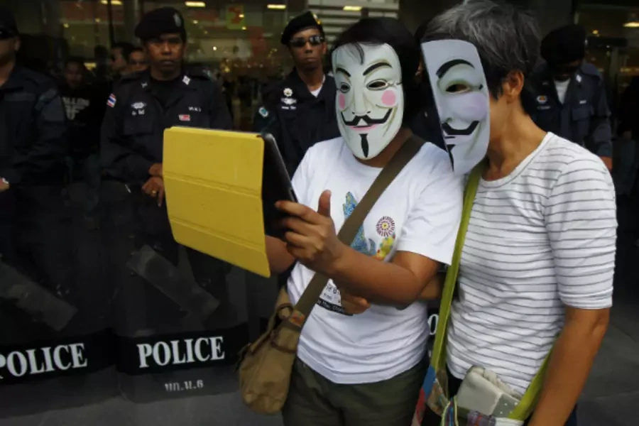 Anti-government protesters wearing Guy Fawkes masks use an iPad in front of riot policemen during a rally outside a shopping mall in Bangkok on June 9, 2013. (Chaiwat Subprasom/Courtesy Reuters)