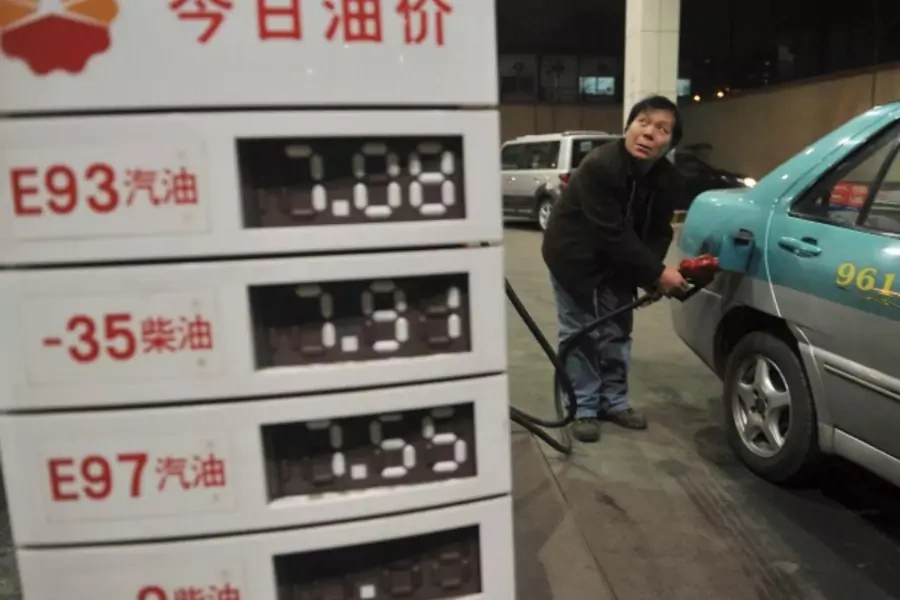 A taxi driver looks at the price as he fills the tank of his car near a board showing recently increased prices at a gas station in Shenyang, Liaoning province, on February 20, 2011. (Stringer/Courtesy Reuters)
