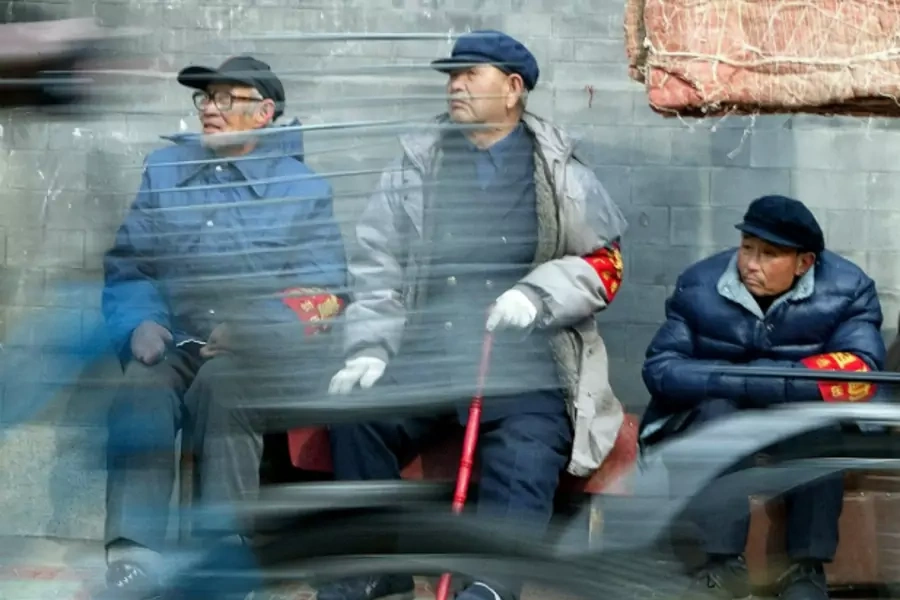 Chinese cyclists ride past three elderly men from neighborhood watch committees in central Beijing on February 27, 2003.