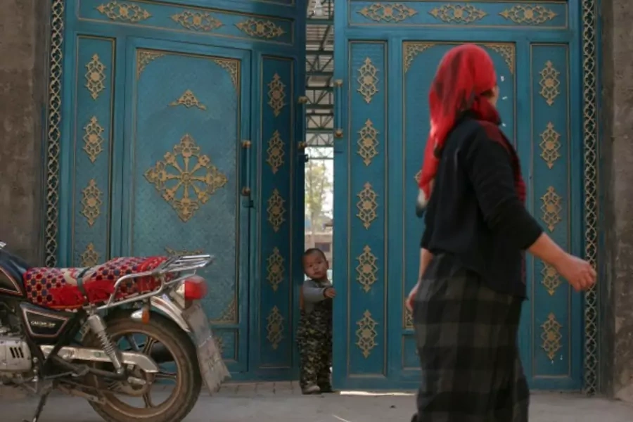 A child looks out from a door as a Uighur woman walks by in a residential area in Turpan, Xinjiang Uighur Autonomous Region on October 31, 2013 (Michael Martina/Courtesy Reuters).