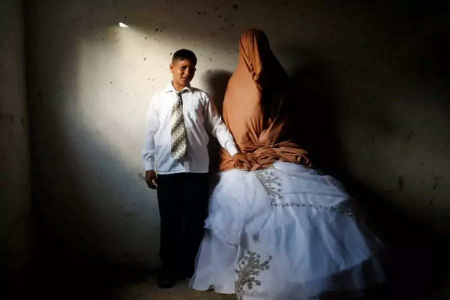 Ahmed Soboh, age 15, stands next to his bride Tala, age 14, inside Tala's house in the town of Beit Lahiya, near the border be...Strip. Ahmed works with his father as a road cleaner earning $5 per day. September 24, 2013 (Courtesy Reuters/Mohammed Salem).