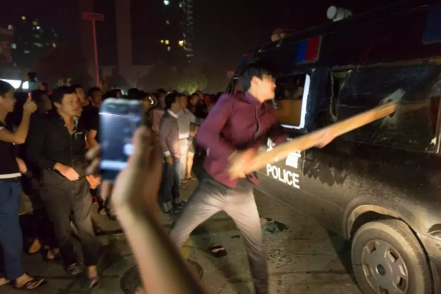 A man breaks the window of a police van with a wooden plank during a protest in Yuyao, Zhejiang province, on October 11, 2013. (Young/Courtesy Reuters)