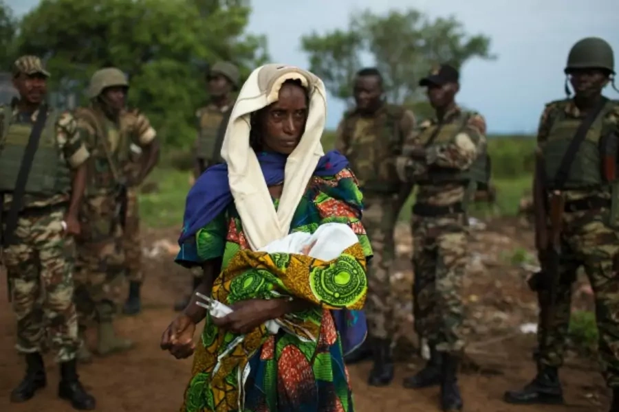 A woman holding a newborn stands in front of African Union troops in the Central African Republic, April 2014 (Courtesy Reuters/Siegfried Modola).