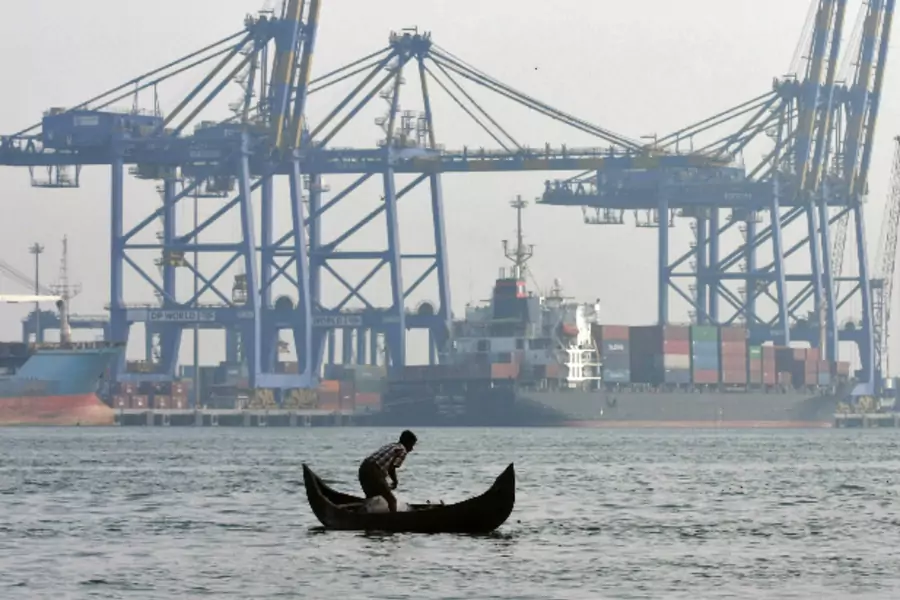 A fisherman prepares to cast his fishing net in the waters of the Vembanad lake as a container ship is seen docked in the background at a port in Vallarpadam, in the southern Indian city of Kochi on February 11, 2014 (Sivaram V/Courtesy: Reuters).