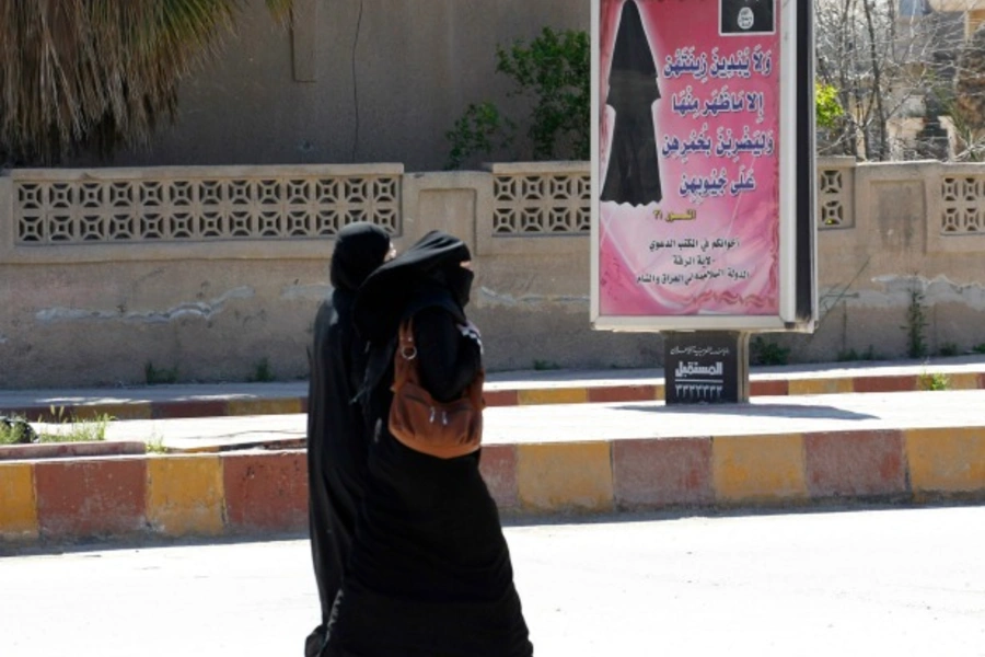 Veiled women walk past a billboard that carries a verse from Koran urging women to wear a hijab in the Islamic State-controlled northern province of Raqqa, Iraq, March 2014 (Courtesy Reuters/Stringer).