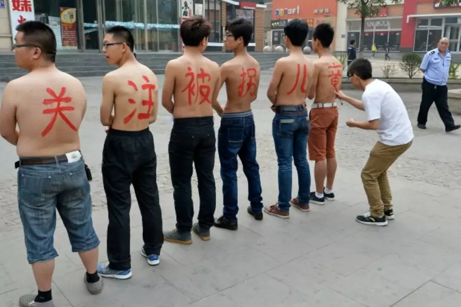 A security guard (R) looks on as a man writes characters on the back of six topless activists with the message "pay attention ...hildren abduction and trafficking, in Taiyuan, Shanxi province May 18, 2013. REUTERS/Jon Woo (CHINA - Tags: CRIME LAW SOCIETY)