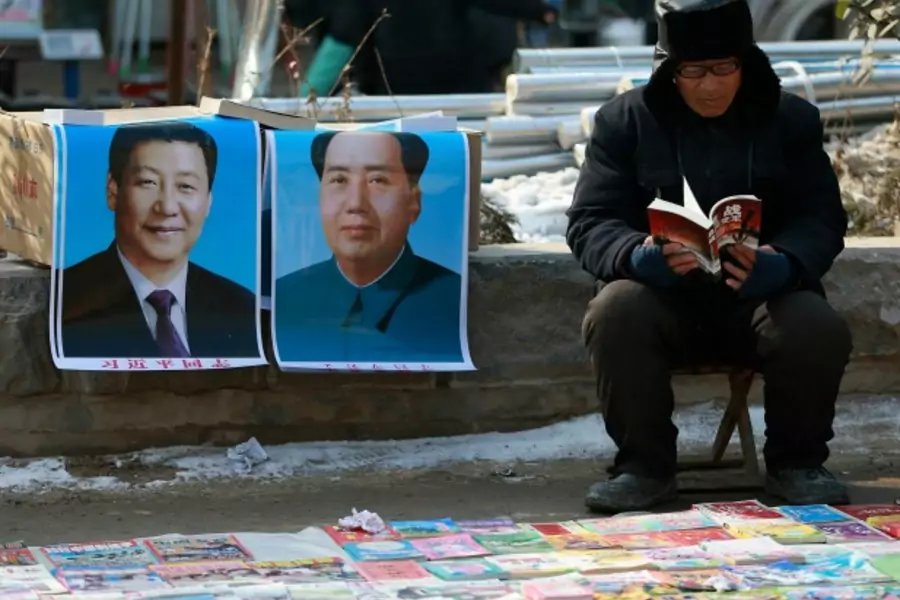 A book vendor reads a book as he waits for customer next to portraits of Chinese President Xi Jinping (L) and late Chairman Ma...vince January 30, 2015. REUTERS/Stringer (CHINA - Tags: SOCIETY POLITICS) CHINA OUT. NO COMMERCIAL OR EDITORIAL SALES IN CHINA