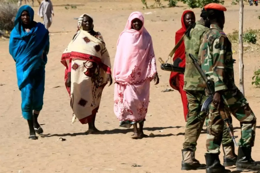 Military personnel walk past women in Tabit village in North Darfur, Sudan. The joint peacekeeping mission in the region known...2014 to investigate media reports of an alleged mass rape of 200 women and girls (Courtesy Mohamed Nureldin Abdallah/Reuters).