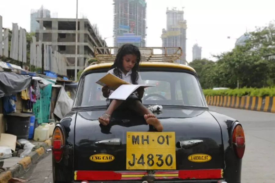 A girl studies while sitting on top of a taxi outside her shanty home at a roadside in Mumbai, India (Shailesh Andrade/Reuters).