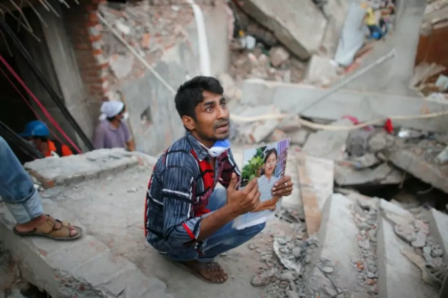 A relative holds up a picture of a garment worker in front of the rubble of the collapsed Rana Plaza building (Reuters/Andrew Biraj).