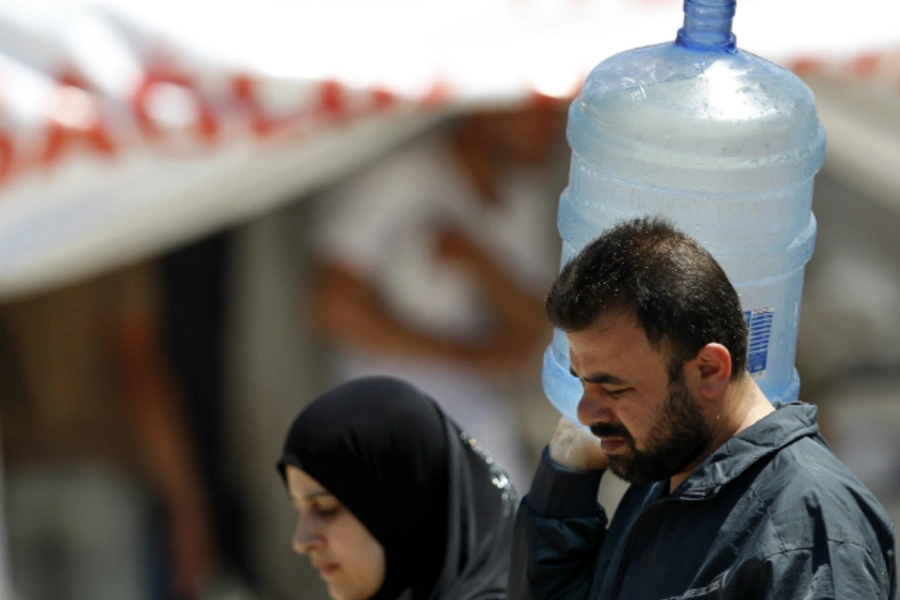 A Syrian man carries a water container as he is accompanied by a woman at a refugee camp in the Turkish border town of Yayladagi (Reuters/Umit Bektas)