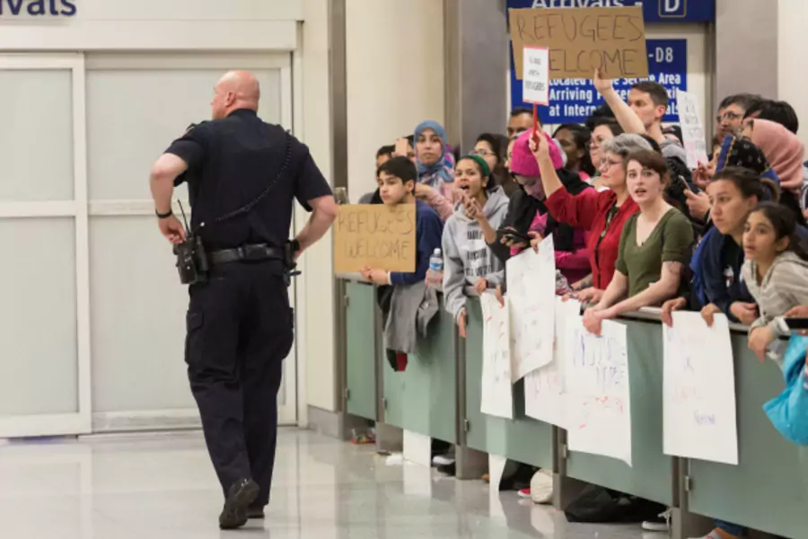 A police officer walks past people as they gather to protest against the travel ban imposed by U.S. President Donald Trump's executive order, at Dallas/Fort Worth International Airport in Dallas, Texas (Laura Buckman/Reuters).
