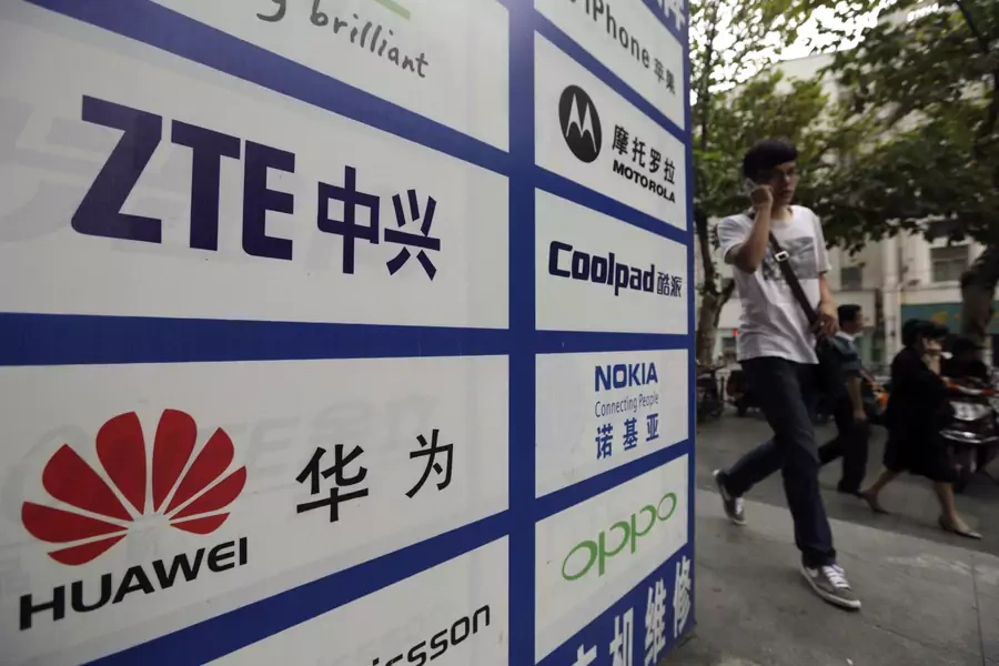 A man walks past an advertisement board showing the logos of Huawei and ZTE outside a mobile phone repair shop in Wuhan, China. Huawei and ZTE have been active participants in building the digital new silk road.