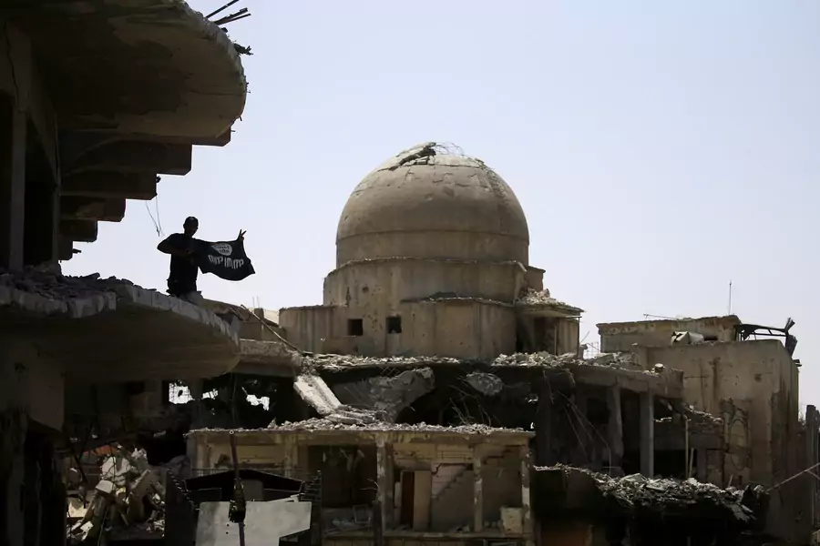 A member of Iraqi security forces holds an upside-down Islamic State flag on top of a building destroyed from clashes in the Old City of Mosul, Iraq (Thaier Al-Sudani/Reuters).