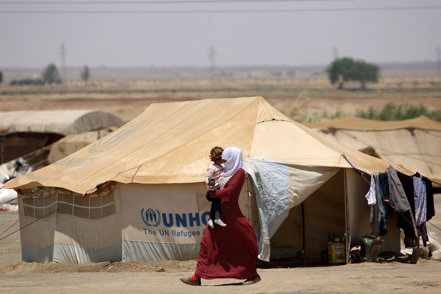 A Syrian woman displaced from Raqa walks carrying a child at the al-Karamah camp