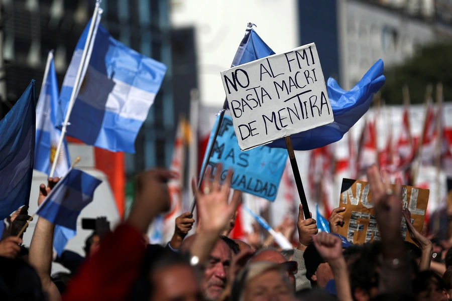 People walk past a grafitti that reads "IMF (International Monetary Fund), never again" during a demonstration to demand jobs and social benefits in Buenos Aires, Argentina, June 1, 2018.