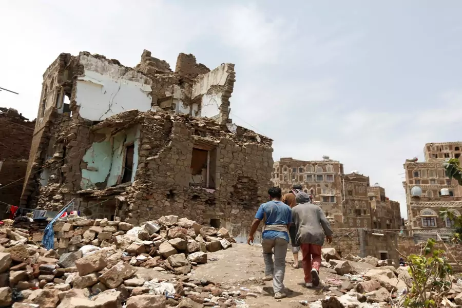 People walk past a house destroyed by an air strike in the old quarter of Sanaa, Yemen on August 8, 2018.