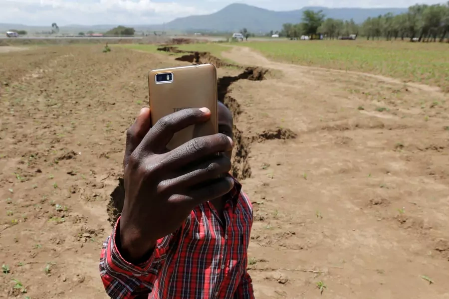 A man holds his phone to take a Facebook live video near a chasm suspected to have been caused by a heavy downpour along an underground fault-line near the Rift Valley town of Mai Mahiu, Kenya March 28, 2018.
