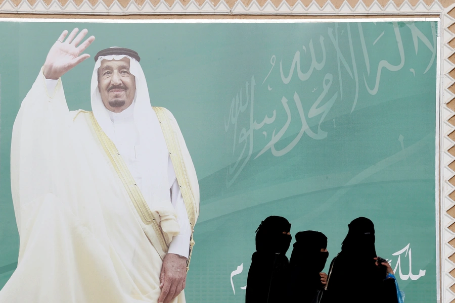 Women walk past a poster of Saudi Arabia's King Salman bin Abdulaziz Al Saud.