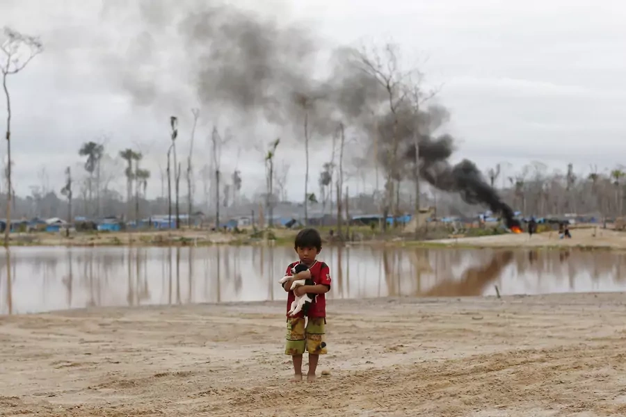 A boy carries a dog as he stands after a Peruvian police operation to destroy illegal gold mining camps in the southern Amazon region of Madre de Dios on July 14, 2015. 