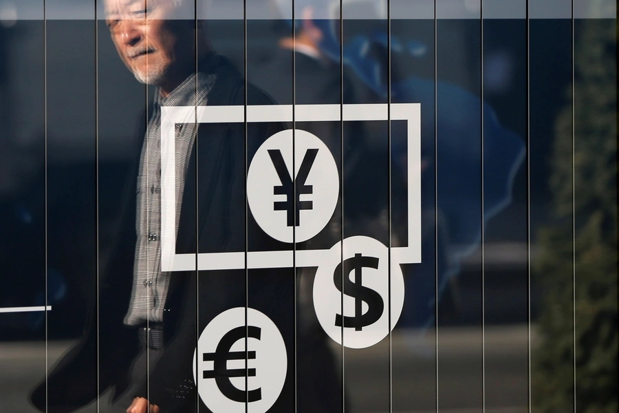 Passers-by are reflected on a signboard displaying currency signs outside a bank in Tokyo November 27, 2014. 
