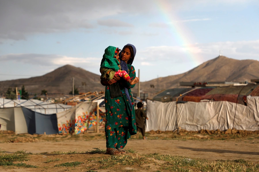 An internally displaced Afghan girl carries a child near their shelter at a refugee camp on the outskirts of Kabul, Afghanistan, on June 20, 2019.