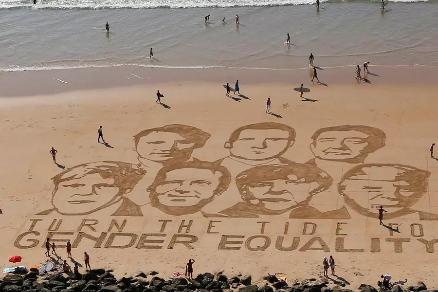 The faces of the G7 leaders are drawn in sand with the message "Turn the Tide for Gender Equality."