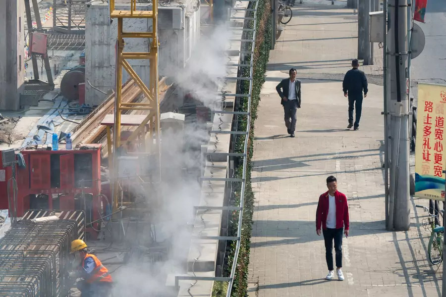Men walk by a construction site, separated by a wall installed with water misting system for dust control, in Shanghai, China April 8, 2019.