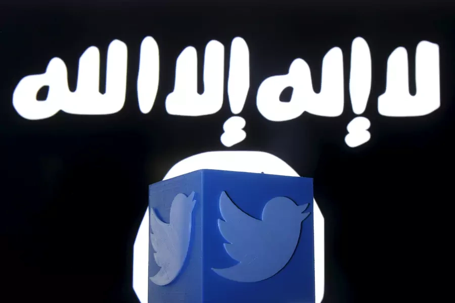 A 3D-printed Twitter logo is seen in front of a computer screen on which an Islamic State flag is displayed.