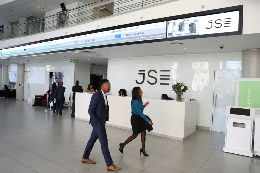 Visitors walk past a reception with an electronic board displaying movements in major indices at the Johannesburg Stock Exchange building in Sandton, Johannesburg, South Africa, August 22, 2019.