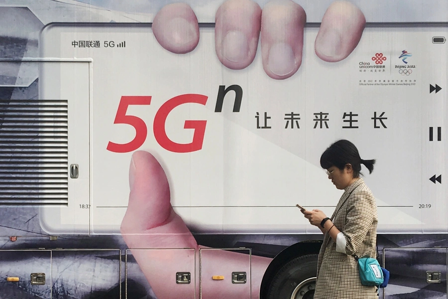 A woman using her mobile phone walks past a vehicle covered in a China Unicom 5G advertisement in Beijing, China September 17, 2019.