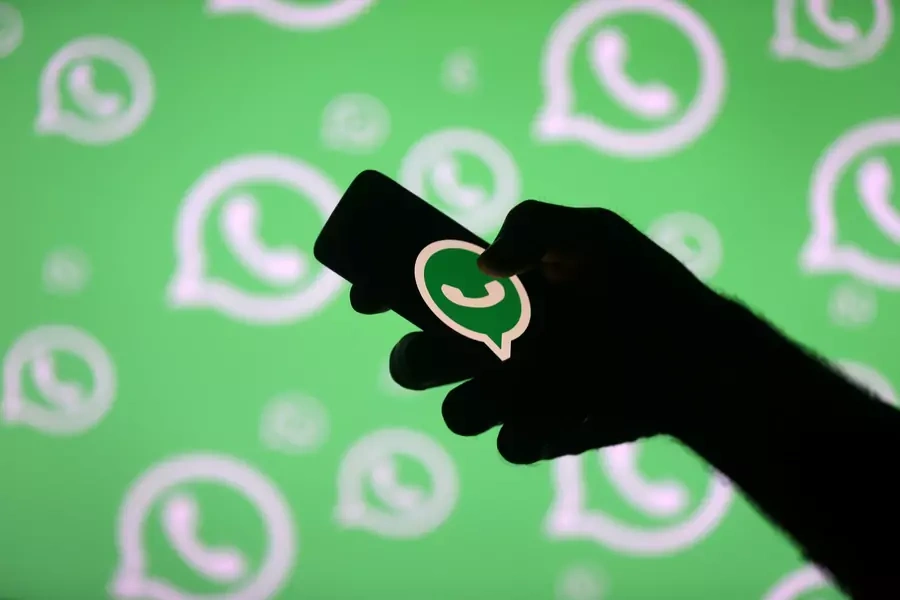 A man poses with a smartphone in front of displayed Whatsapp logo in this illustration