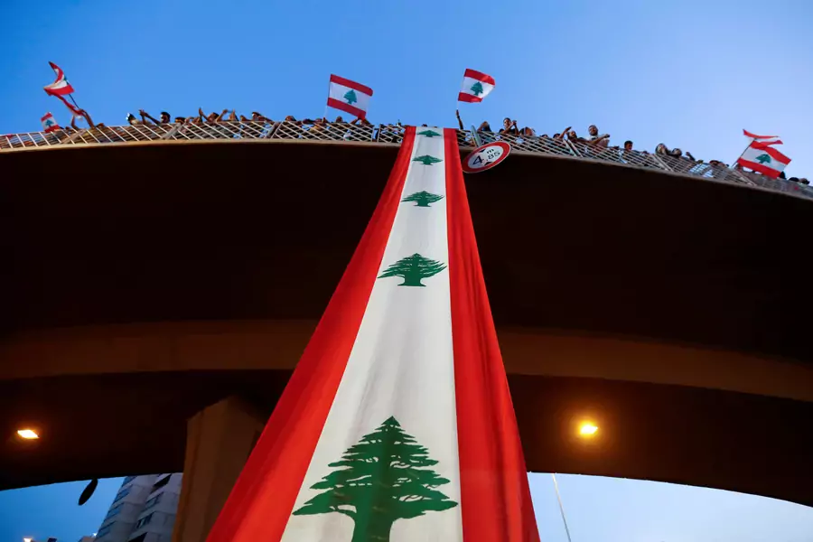Demonstrators stand on a bridge decorated with a national flag during an anti-government protest along a highway in Lebanon, on October 21, 2019.