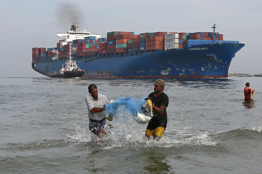 Fishermen carry bluefin trevally fish, locally known as Vatta, as a cargo ship carries containers in the Arabian Sea off Kochi, India, on May 9, 2018. 