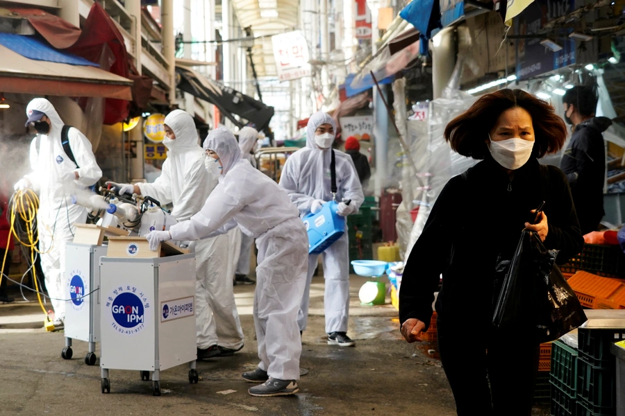 A woman wearing a mask to prevent contracting the coronavirus reacts as employees from a disinfection service company sanitize a traditional market in Seoul, South Korea, on February 26, 2020.