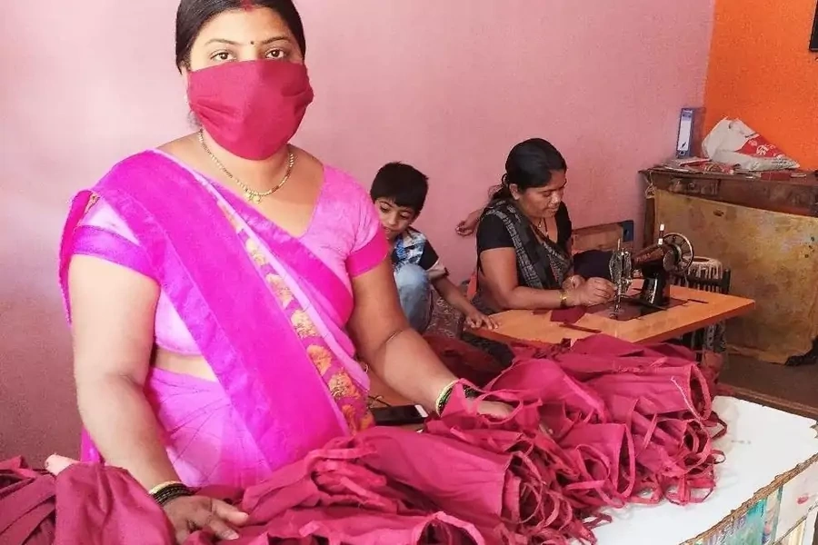 Woman stands behind face masks sewn by members of the Self-Employed Women’s Association (SEWA) in India.