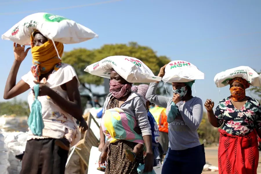 Women carry bags of maize as people queue to receive food aid amid the spread of the novel coronavirus, near Pretoria, South Africa, on May 20, 2020.