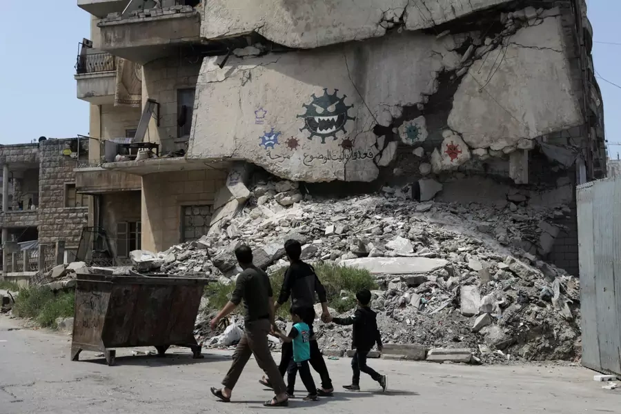 People walk by a damaged building on which illustrations of the novel coronavirus have been spray painted in Idlib, Syria, on April 18, 2020.