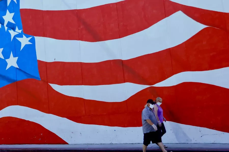 Two people in masks walk by a mural of the U.S. flag in Ocean Beach, California.